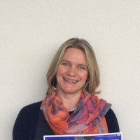 Abigail Aikenhead, a woman with a blonde bob wearing a navy top and pink scarf.