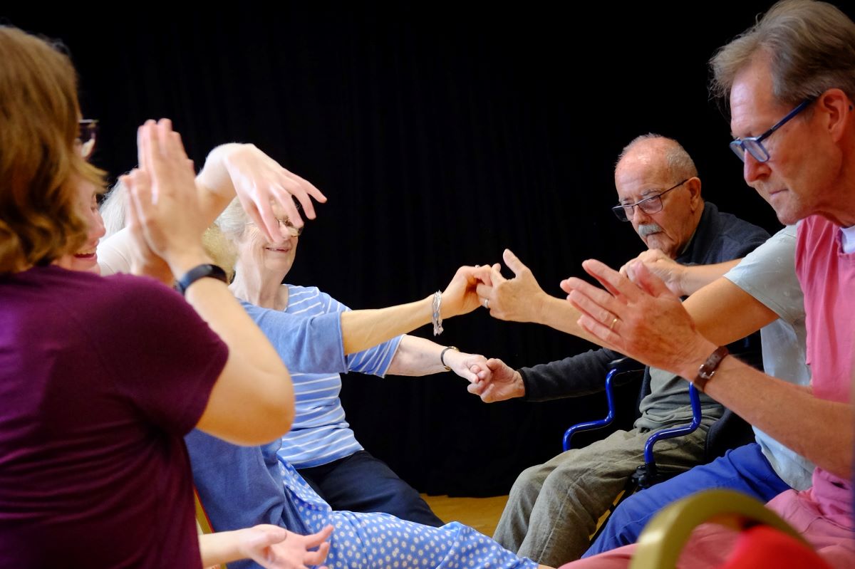 People seated in a circle moving arms and touching hands
