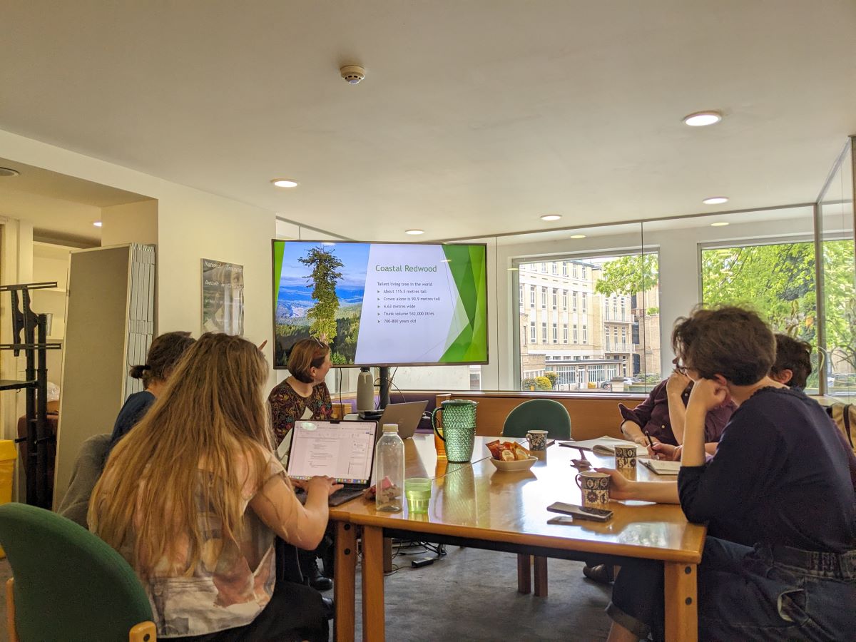A group of people sit around a table looking at a screen.