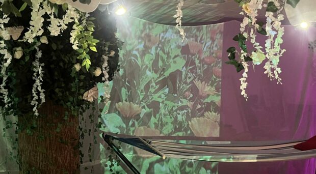 A close up of the Happy Place installation with a floral projection on the wall, hammock and fabric and foliage hanging from the ceiling.