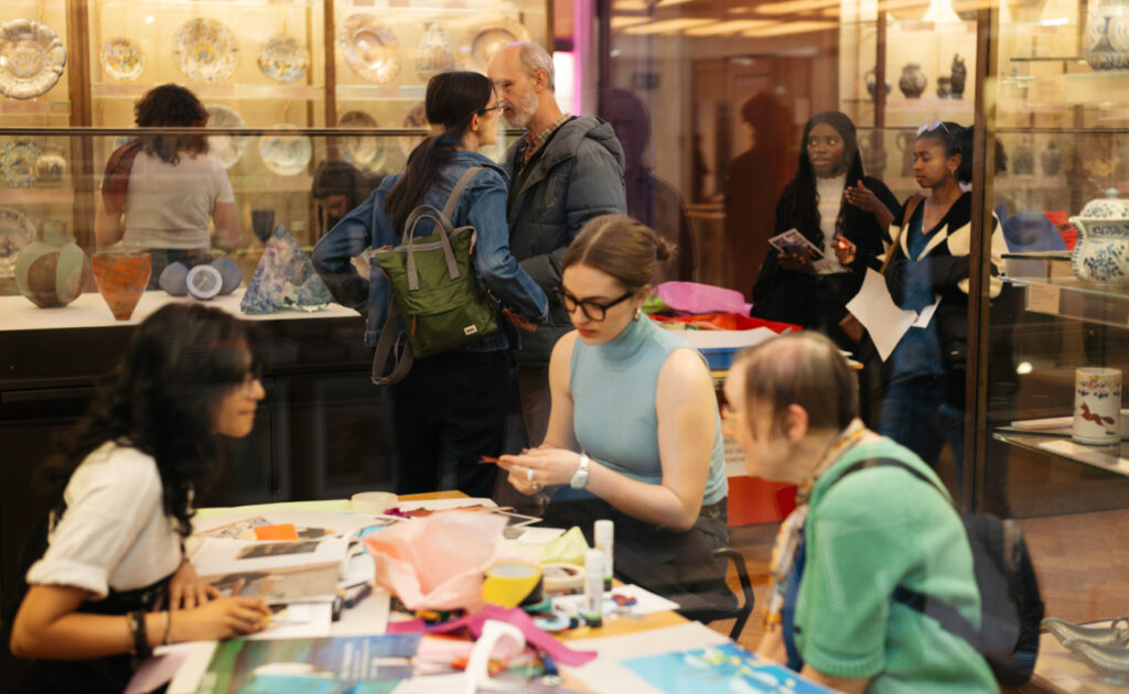 A Fitzwilliam Museum gallery full of people, with three sat around a table in the foreground taking part in craft activities.