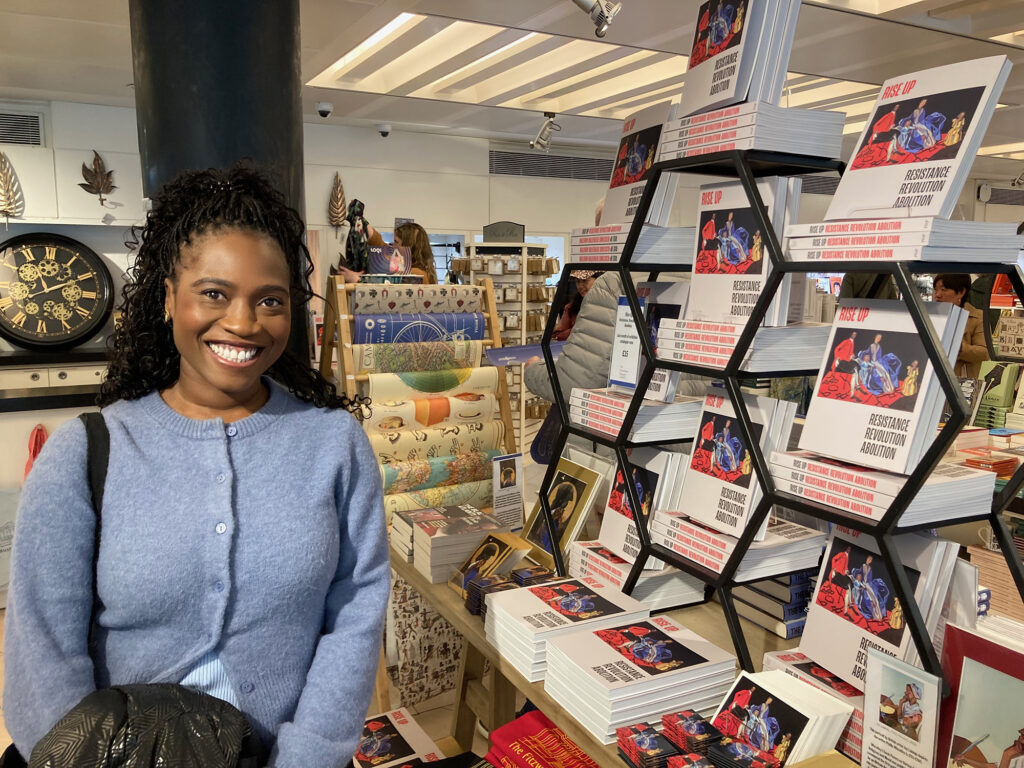 Joy Labinjo smiles next to the display of the Rise Up catalogue featuring her portrait in the Fitzwilliam Museum shop.