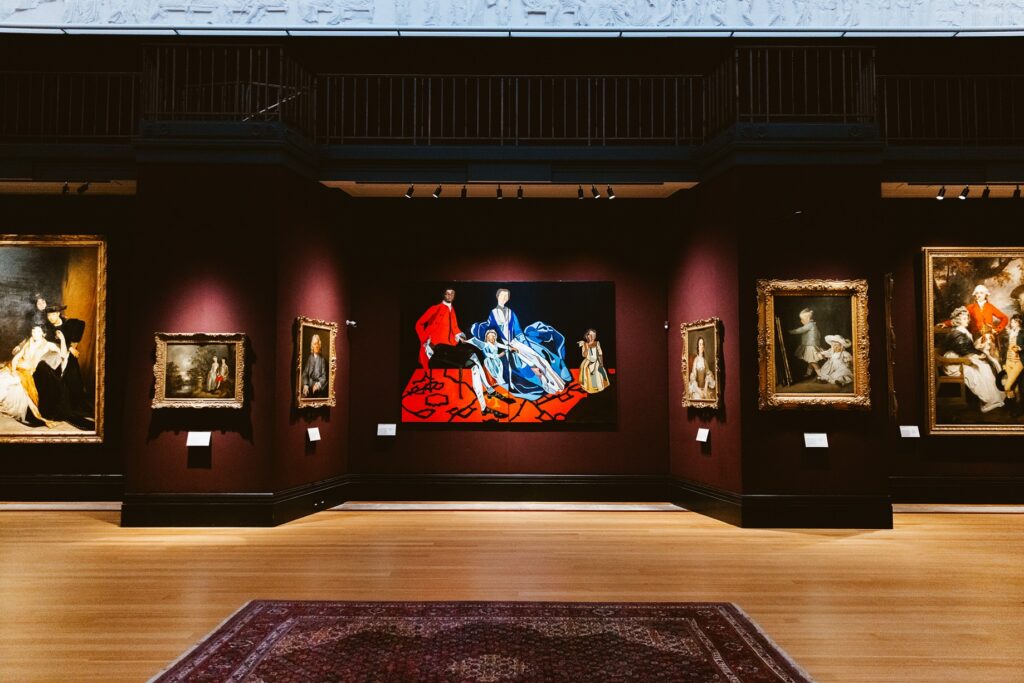 Seen from a distance Joy Labinjo’s An Eighteenth-Century Family in the centre of the dark-walled Gallery 3 in the Fitzwilliam Museum.