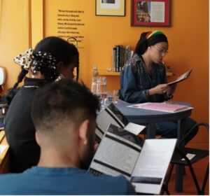 Jade Pollard-Crowe sits reading from their ‘Olaudah Equiano: A Cambridgeshire History Zine’ in front of others during their Zine-making Workshop in the Rise Up Reflection Space.