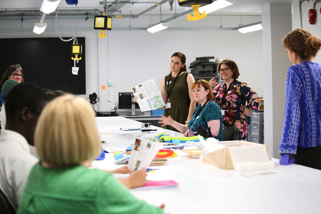 Four women members of museum staff stand on one side of a table filled with museum objects at the Centre for Material Culture.