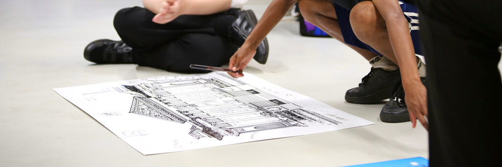 Work experience students draw on an illustration of the Fitzwilliam Museum, which is placed on the floor.