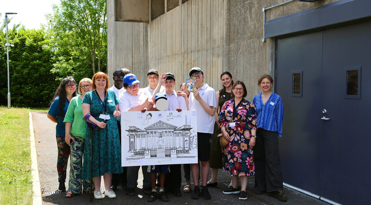 The group of students and staff standing outside the Centre for Material Culture holding a large illustrated drawing of the Fitzwilliam Museum.