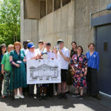 The group of students and staff standing outside the Centre for Material Culture holding a large illustrated drawing of the Fitzwilliam Museum.