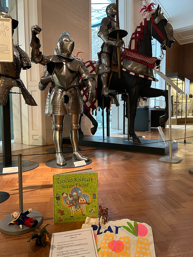 A Story Starter Pack, including Play tote bag, storybook, toys and instruction sheet, laid out on the wooden floor of the armoury gallery.