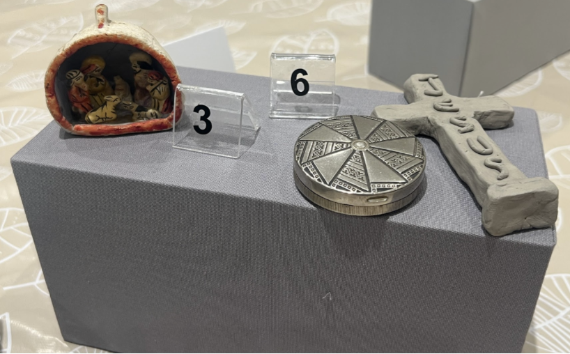 A grey stand with three objects resting on tip, and two numbers 3 and 6, showing personal items and creations by the group.