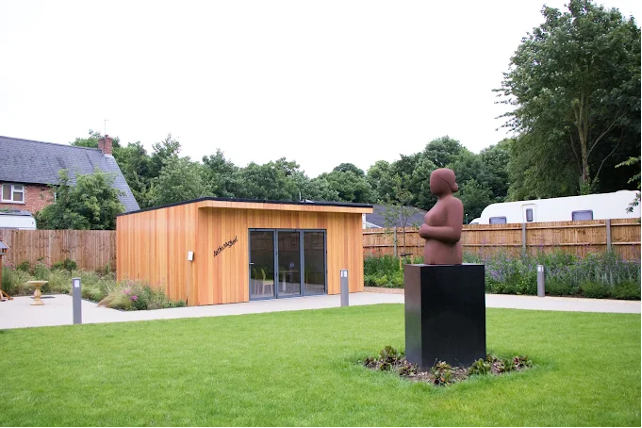 The garden of the Arthur Rank Hospice with green lawn, statue and the wooden clad Arthur's Shed building.