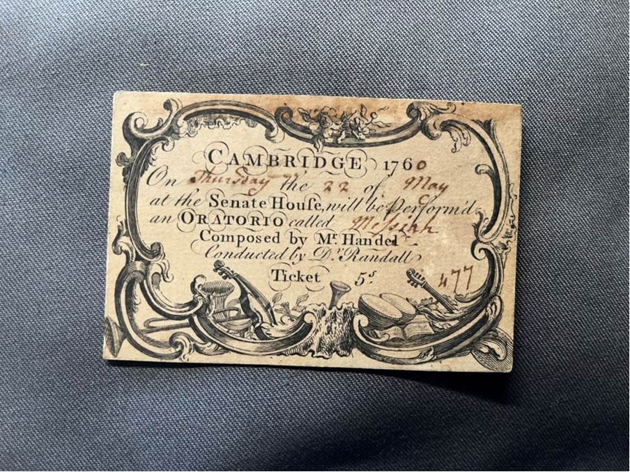 A small rectangular ticket of paper with a border filled with musical instruments and central text reading Cambridge 1760, On Thursday the 22 of May at the Sentra House will be perform'd an oratorio called Messiah composed by Mr Handel conducted by Dr Randall, Ticket 5s, 477.