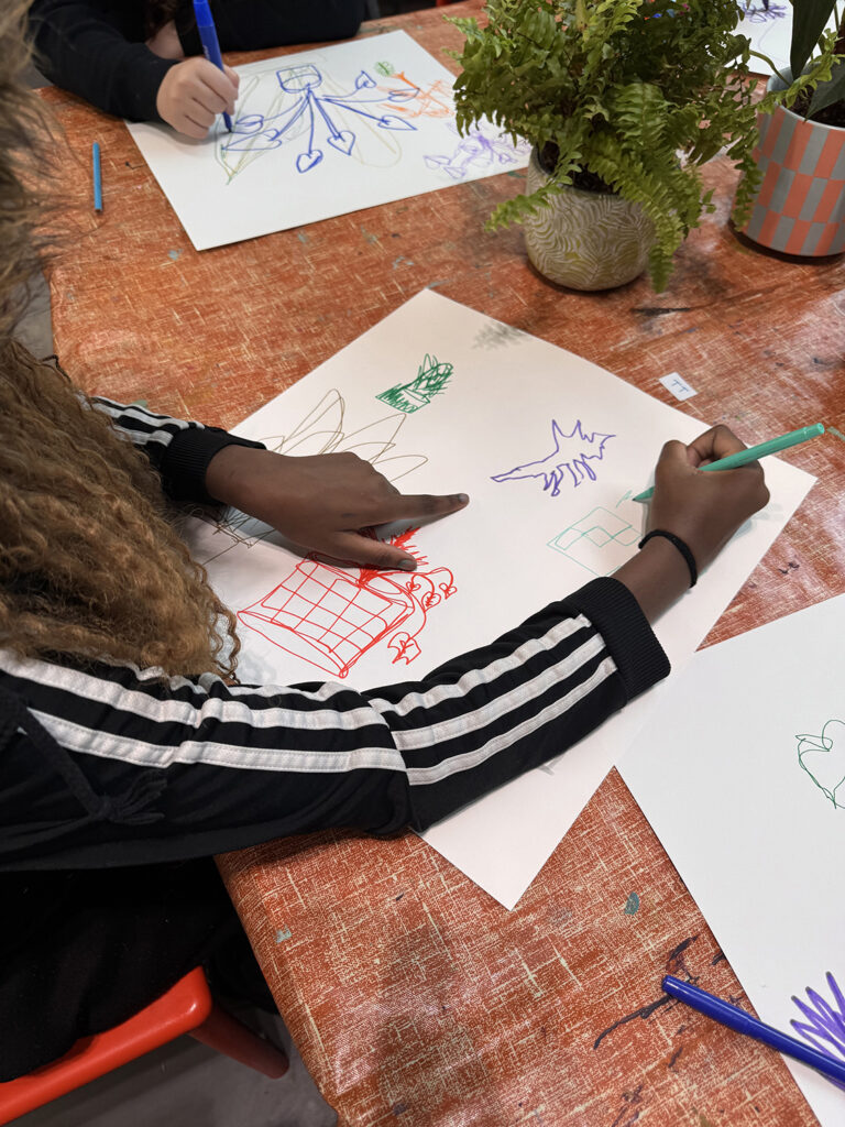 Two young people lean on a table drawing line drawings on A3 paper with felt tips.