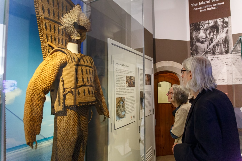 Two visitors look at a display of armour from Kiribati