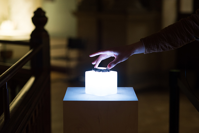 Photograph of a hand reaching out to touch an artefact on an illuminated cube.