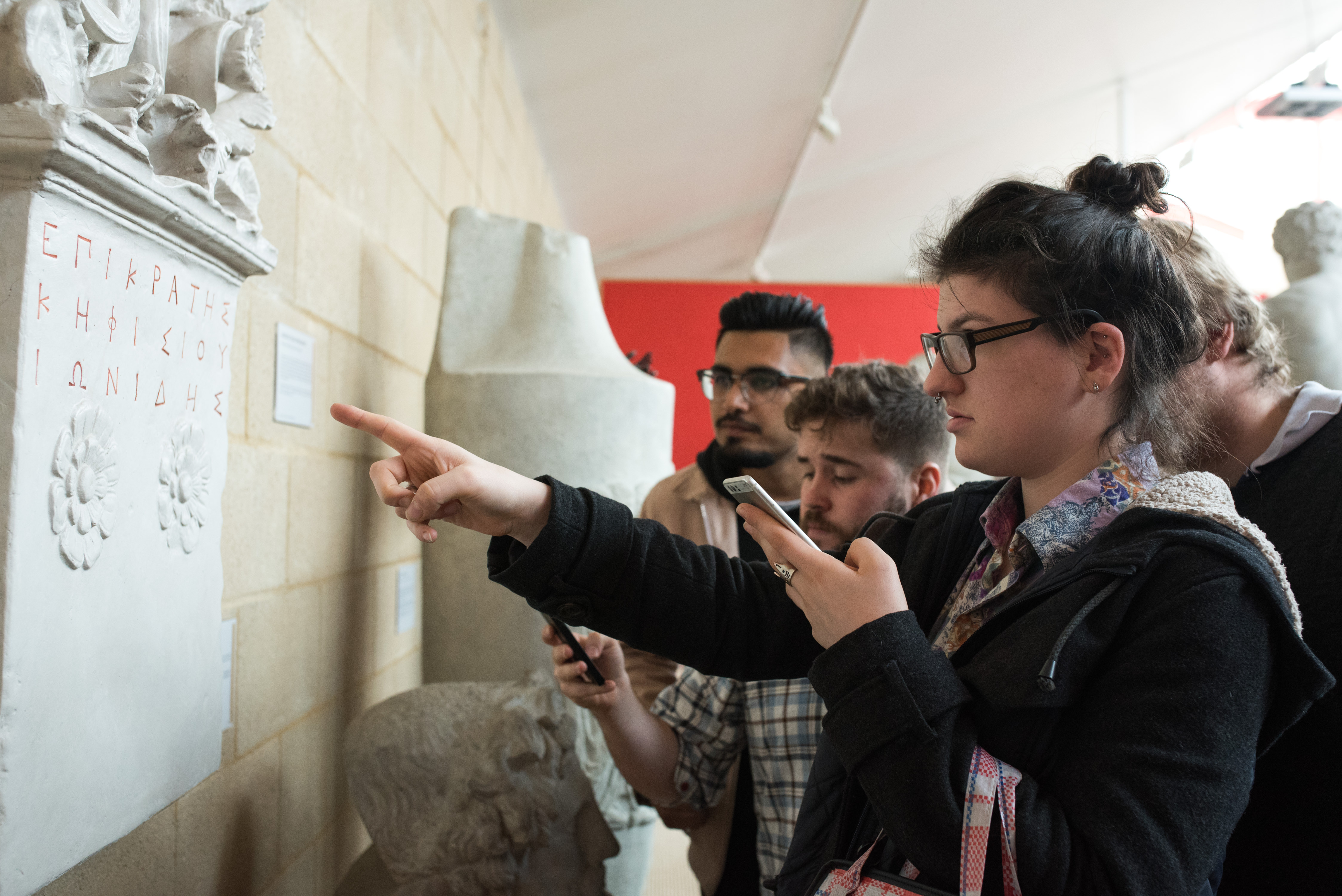 Four players holding their phones look closely at an inscription on the wall of the Museum of Classical Archaeology