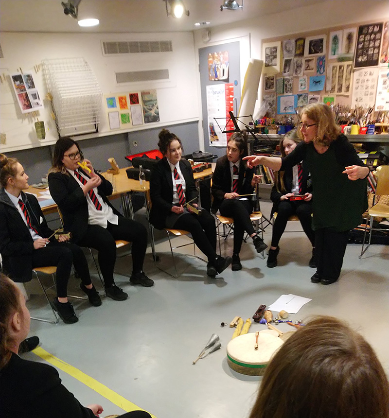 Students sit in a circle and experiment with different musical instruments, including recorders and drums