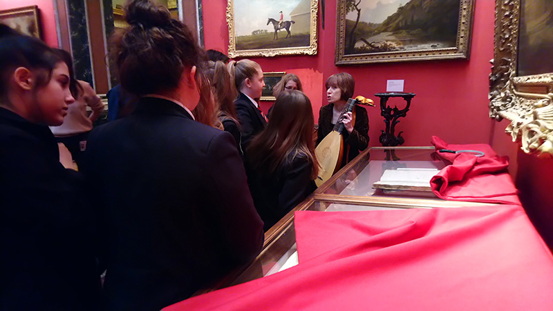 Students gather around a curator holding a lute