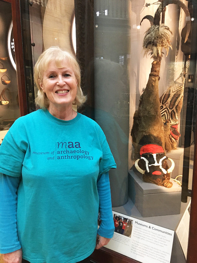 Gloria, a fair-haired lady dressed in a blue MAA tshirt, stands in front of one of the Pacific Islands display cases