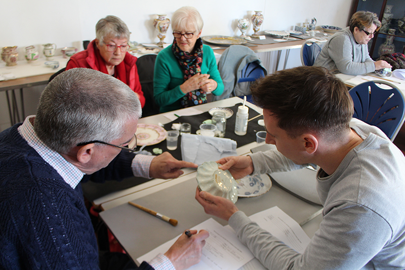 View over the shoulders of Tim and a volunteer as they look closely at a dish