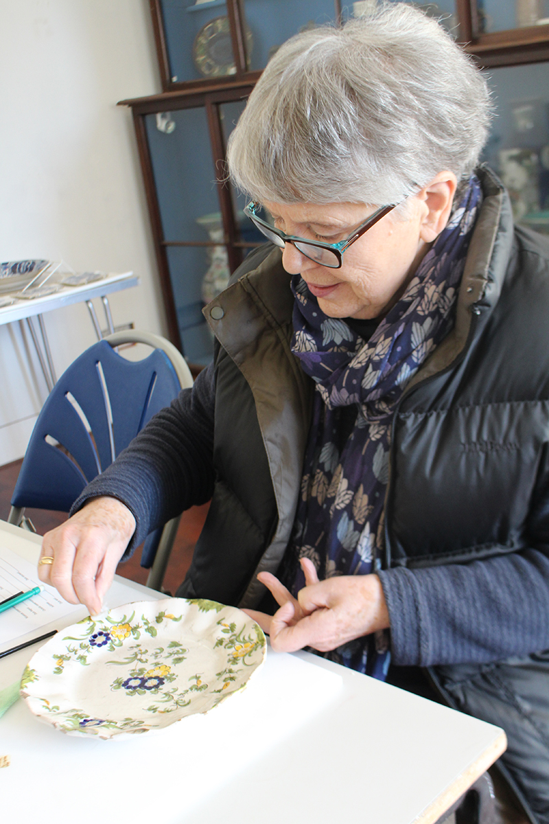 A volunteer wet-cleaning a dish with a delicate floral pattern with a damp swab