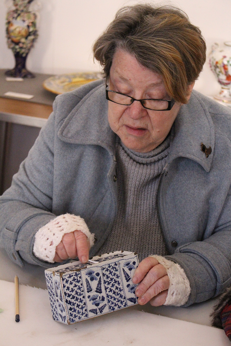 A volunteer cleaning a blue and white Delftware flower brick with a cotton bud. The brick is slightly chipped along its edges.