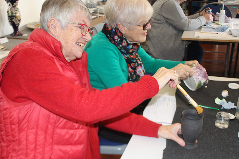 A volunteer dry-cleaning a black basalt vase with a brush whilst her neighbour wet-cleans with a damp swab