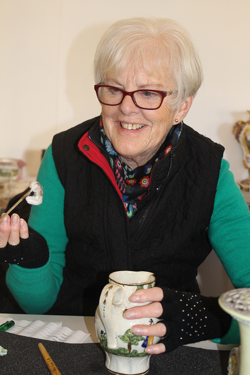 A smiling volunteer steadies a small vase in one hand and holds up a dirty swab in the other