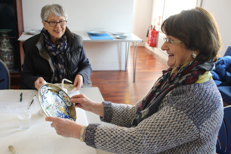 A volunteer admires the gleam on a newly cleaned plate, while a second smiles on