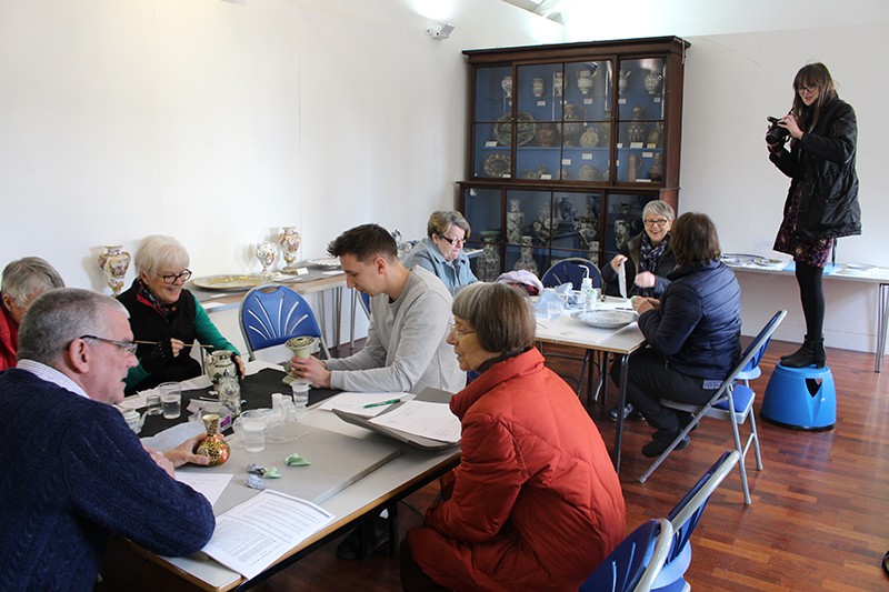 A shot of the room, where the volunteers are hard at work with Tim at the table. Sarah is standing on a stool to take a photo of the scene