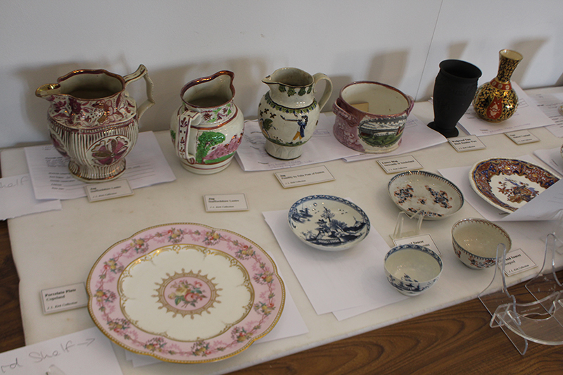 A spread of ceramic plates, jugs, small bowls, laid out on a table with their condition reports tucked beneath them