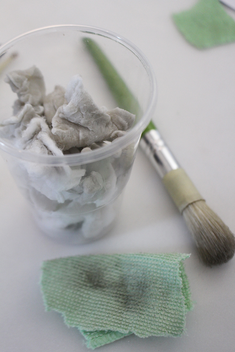 A plastic cup full of dirty cotton swabs, a dirty scrap of microfibre cloth, and a brush