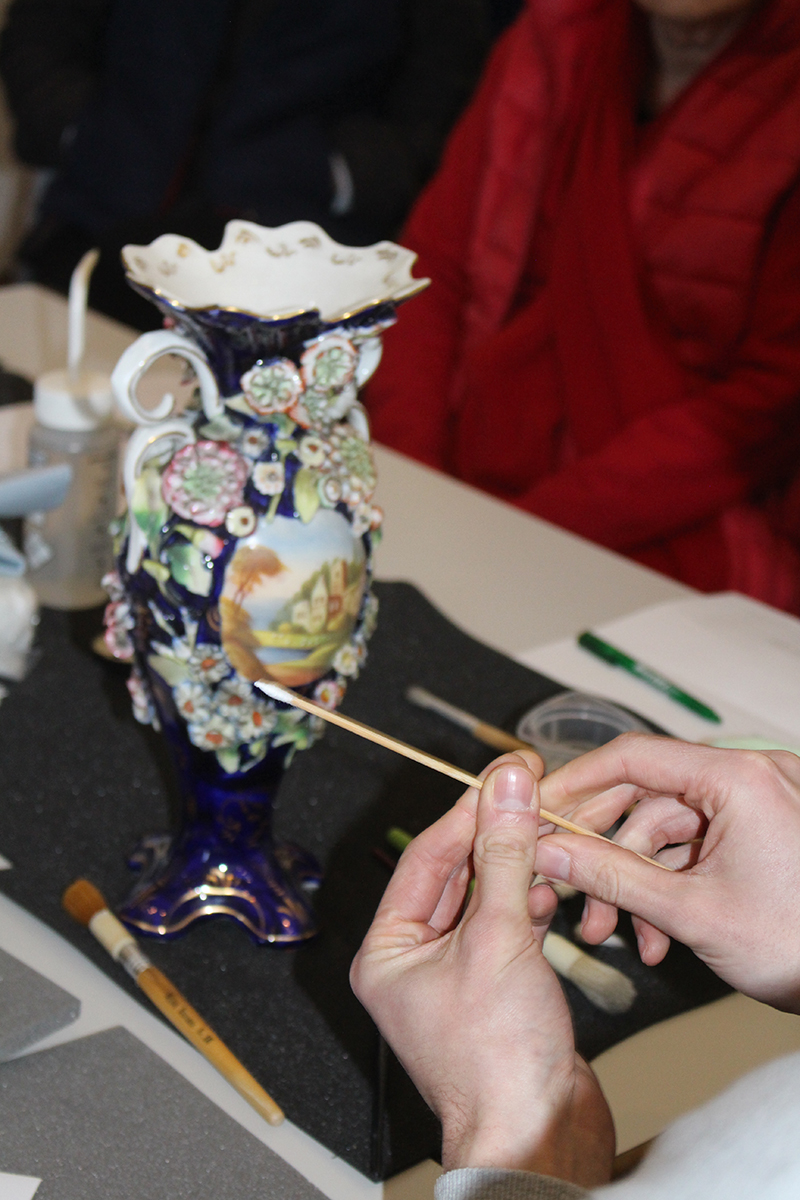 Close up of two hands holding home-made cotton bud, with an elaborate blue and white vase in the background