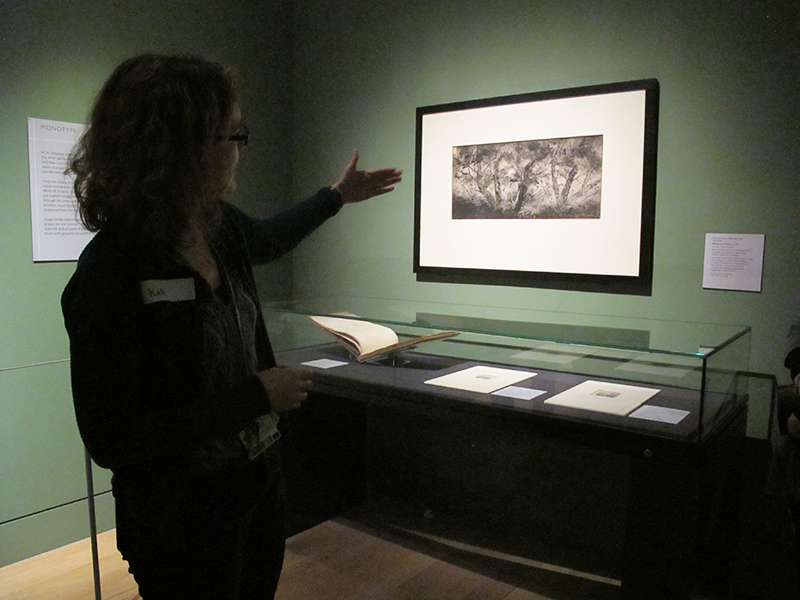 Museum educator Kate gestures to a drawing in a darkened gallery