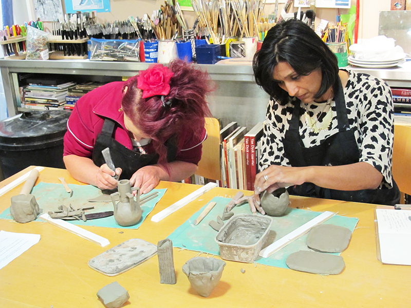 Two teachers dressed in aprons, working with clay in the studio