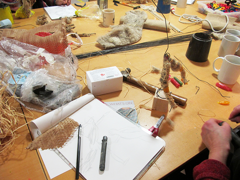 A studio table covered with craft materials, including a model work in progress