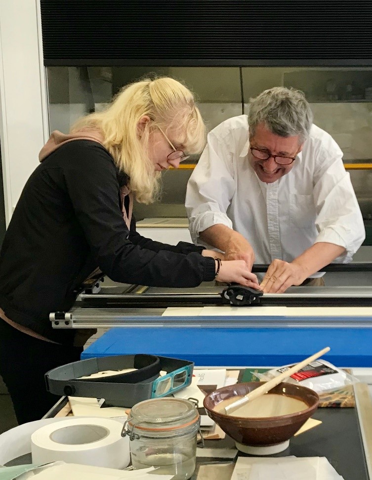 One of the students cuts card using a guillotine with the help of a conservator