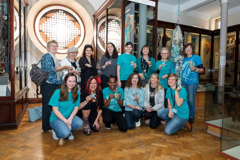 a group of smiling participants hold up their ghost net turtles