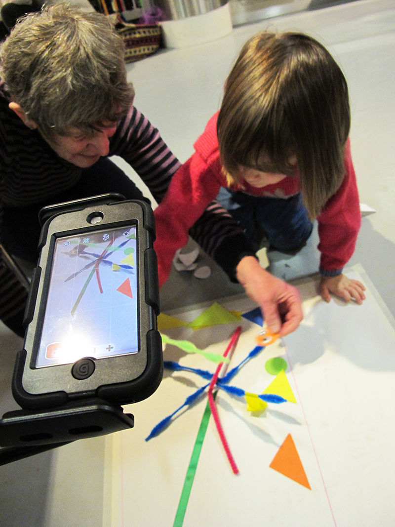 An adult and child work together with colourful shapes to make an animation, using an ipod