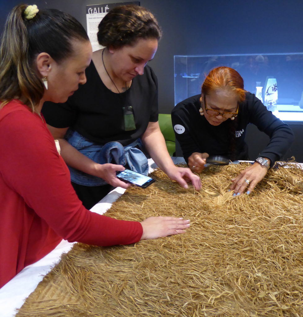 Three women examining a Māori cloak