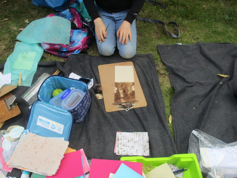 Young people kneeling on grass, learning how to paint nettles