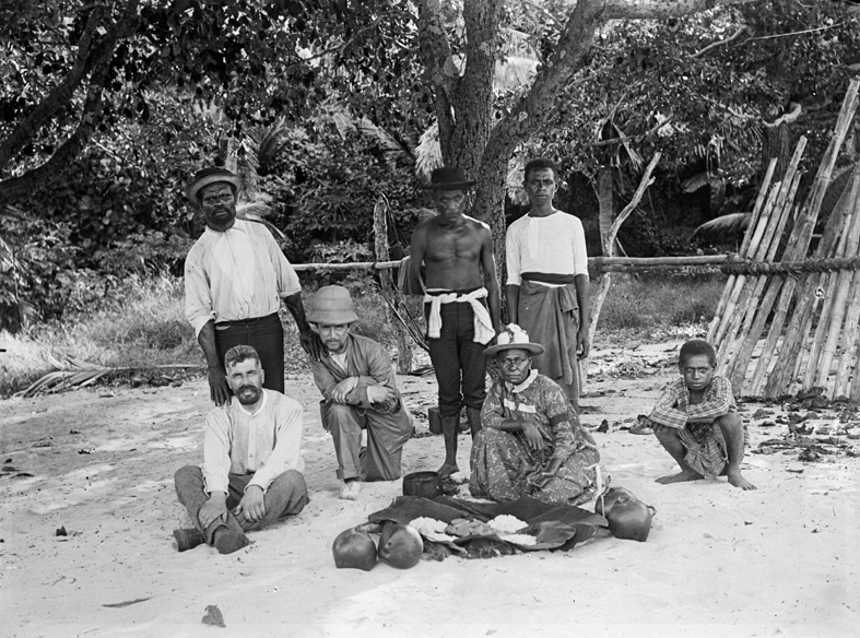 Picnic on the beach with (left to right) Haddon (seated), Pasi, Ray, probably Koriba, Mrs Canoe, unknown youth, and Poi Pasi (squatting). 14 May 1888.