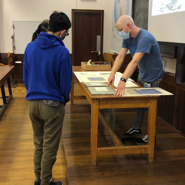 Students look at paintings of polar regions with Collections' Manager Alex Partridge