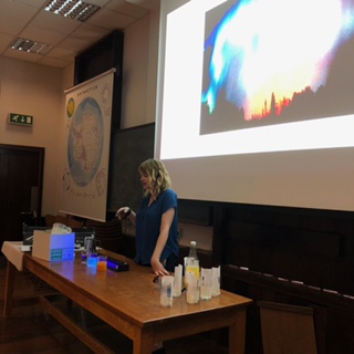 Rosie Amos stands at front of lecture theatre demonstrating experiments