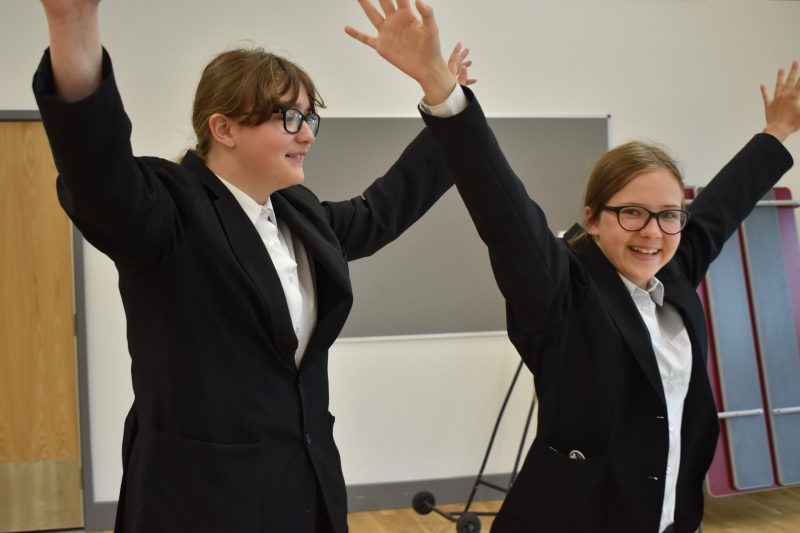 2 young people stand side-by-side with arms outstretched and raised above their heads