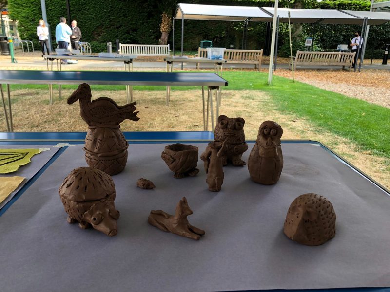 A selection of animal-like clay figures arranged on a table on front lawn of Museum
