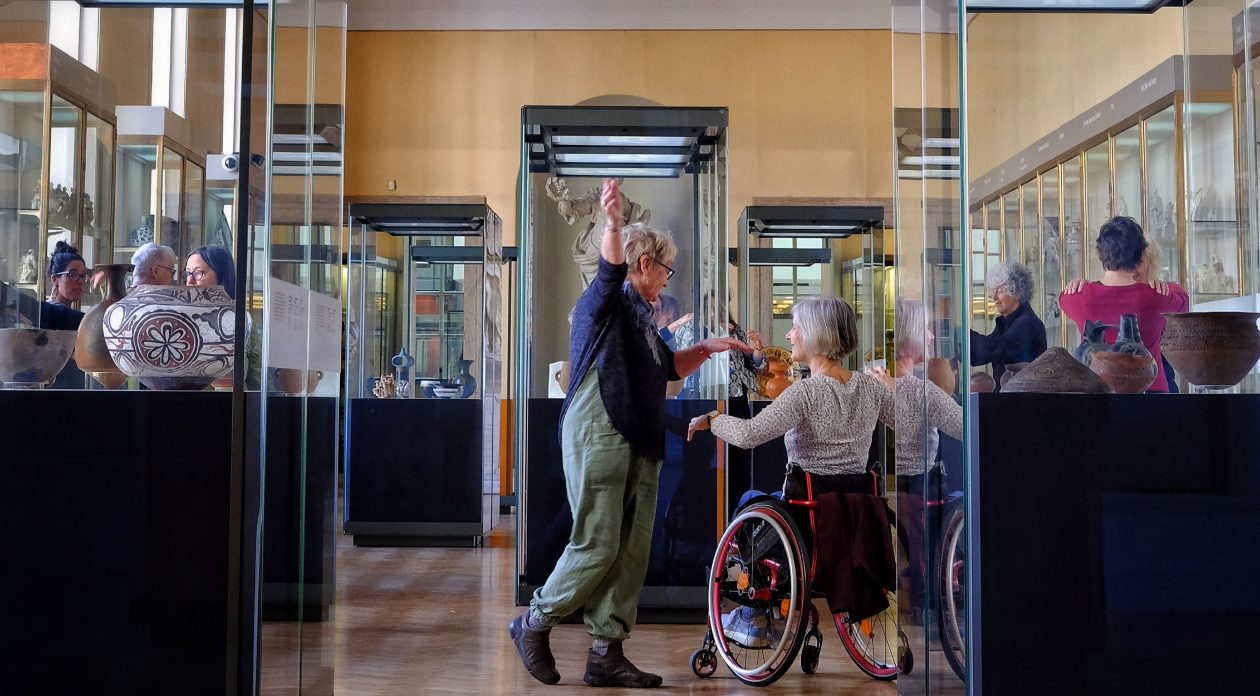Group of older people - one in a wheelchair - in ceramics gallery of the museums surrounded by glass display cabinets