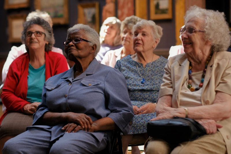 Group of older people sitting in a gallery with a background of paintings