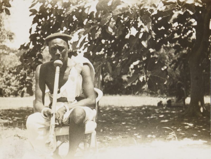 Black and white photograph showing Reth Fafiti Wad Yor seated on a wicker chair near a tree