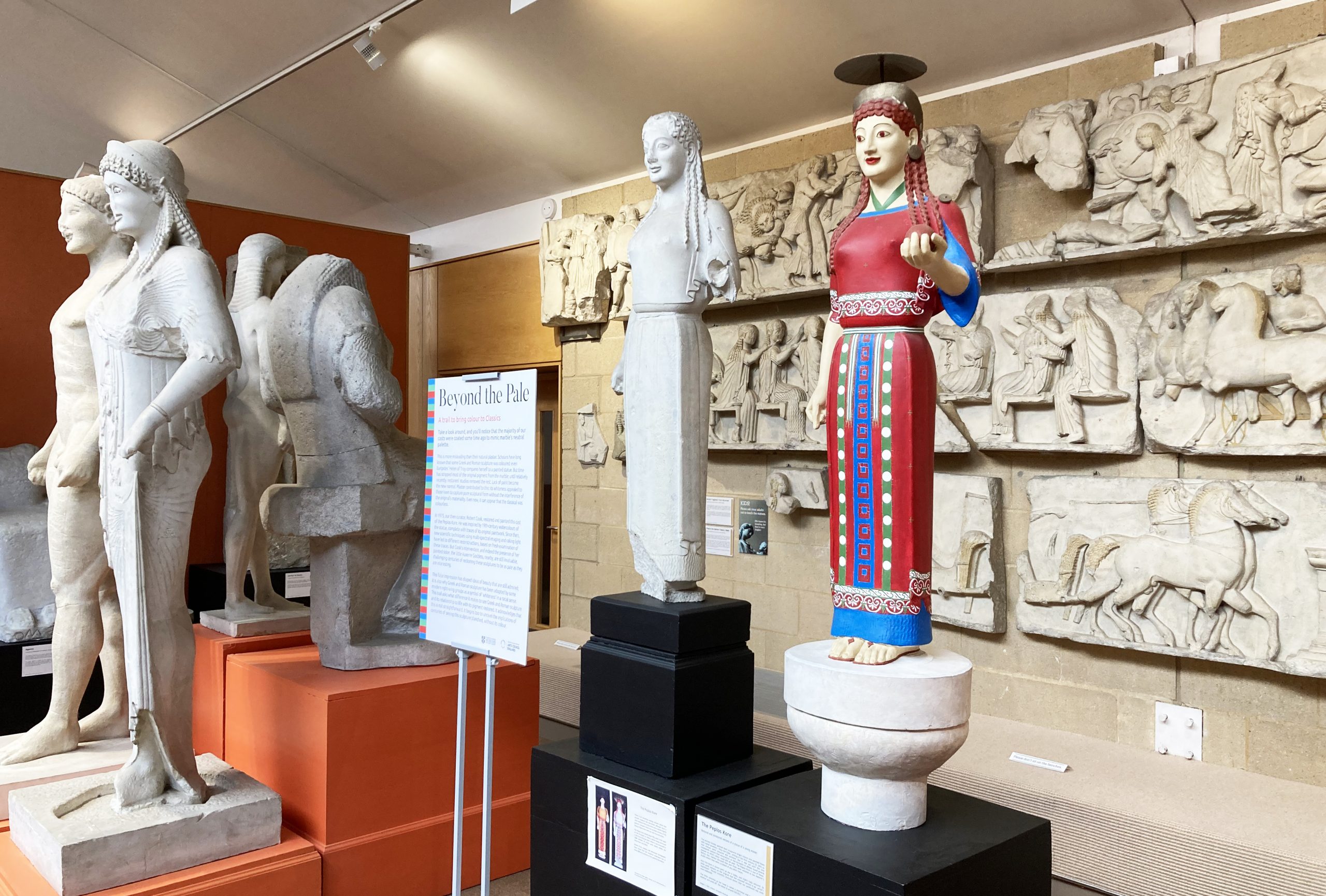 view of the cast gallery where two plaster casts of the same statue are side by side; one is brightly painted and the other white. A new interpretation panel stands next to them.
